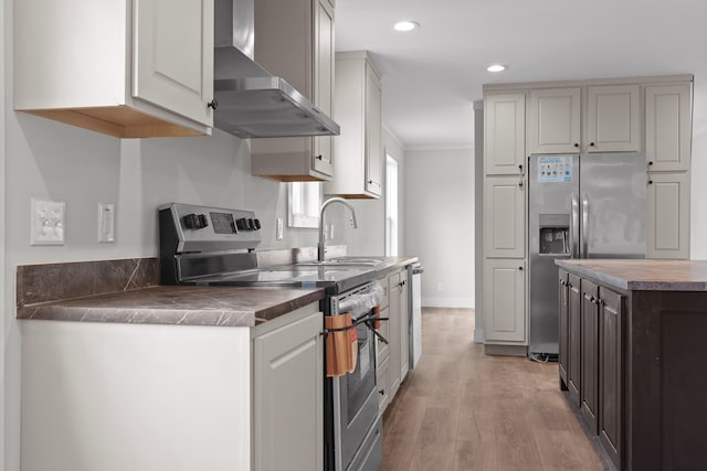 kitchen with sink, light hardwood / wood-style floors, crown molding, wall chimney range hood, and appliances with stainless steel finishes