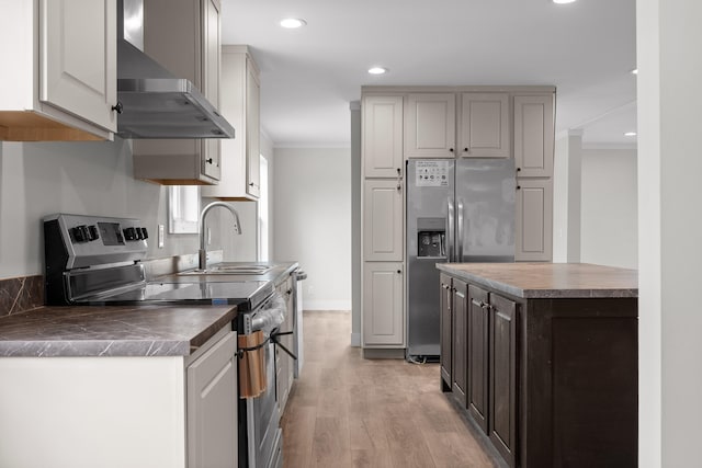 kitchen featuring wall chimney range hood, light wood-type flooring, crown molding, sink, and appliances with stainless steel finishes