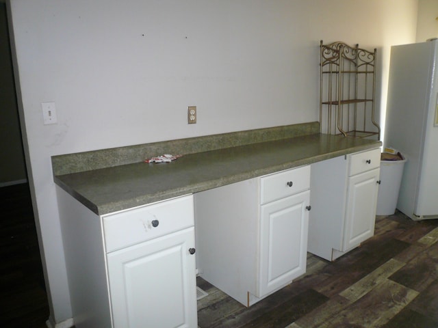 kitchen with white refrigerator, white cabinetry, dark hardwood / wood-style floors, and built in desk