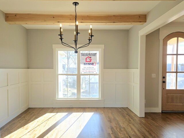 unfurnished dining area featuring beamed ceiling, a chandelier, and light hardwood / wood-style flooring