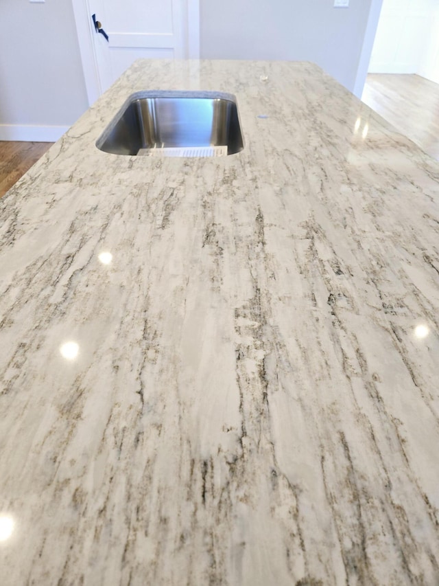 room details featuring light stone counters, sink, and hardwood / wood-style floors