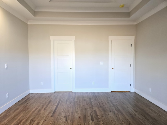 empty room featuring dark wood-type flooring, ornamental molding, and a raised ceiling