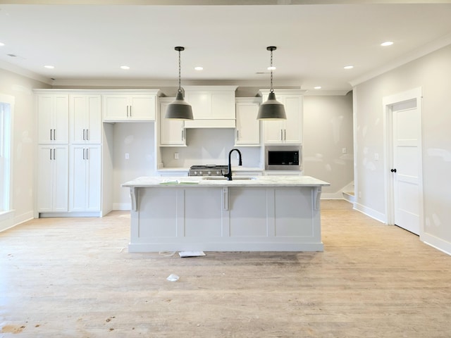 kitchen featuring decorative light fixtures, sink, white cabinets, a center island with sink, and light hardwood / wood-style flooring