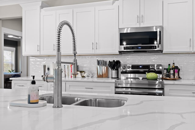 kitchen with white cabinets, tasteful backsplash, stainless steel appliances, and light stone countertops