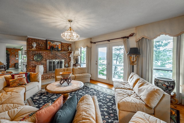 living room with a textured ceiling, wood-type flooring, a notable chandelier, and a brick fireplace