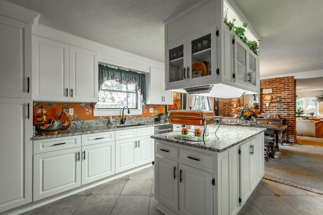 kitchen featuring a textured ceiling, light stone countertops, light tile patterned floors, sink, and white cabinets