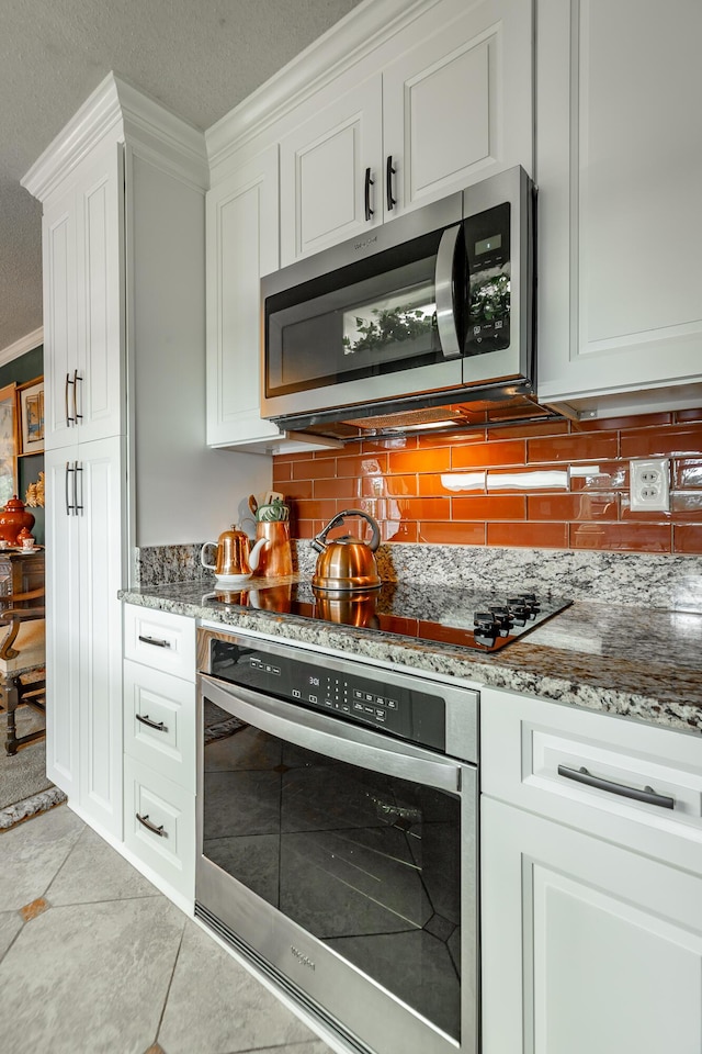 kitchen with ornamental molding, light stone countertops, appliances with stainless steel finishes, white cabinetry, and backsplash