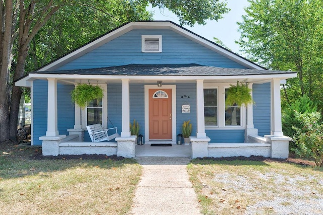 bungalow-style home featuring covered porch, a shingled roof, and a front yard