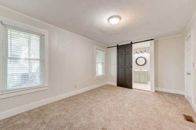 unfurnished bedroom with light carpet, ornamental molding, connected bathroom, and a barn door