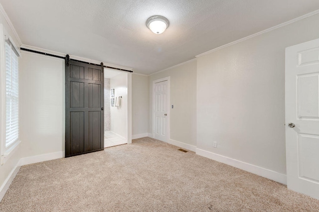 unfurnished bedroom with crown molding, a textured ceiling, a barn door, a closet, and light colored carpet