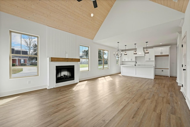 unfurnished living room featuring ceiling fan with notable chandelier, wood ceiling, a fireplace, and light wood-style floors