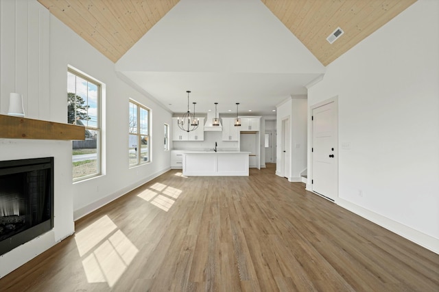 unfurnished living room featuring a large fireplace, baseboards, light wood-style floors, an inviting chandelier, and high vaulted ceiling