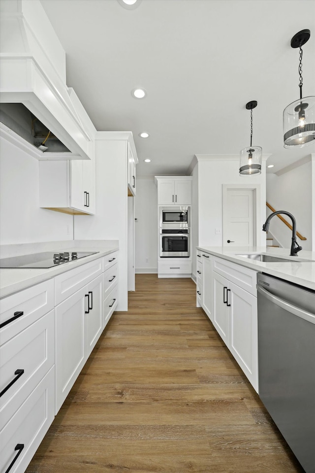 kitchen with premium range hood, light wood-style flooring, a sink, decorative light fixtures, and stainless steel appliances