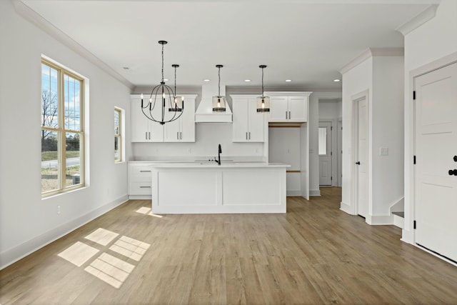 kitchen with light wood finished floors, premium range hood, light countertops, ornamental molding, and white cabinetry