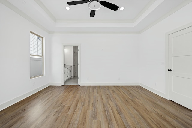 unfurnished room featuring a raised ceiling, recessed lighting, light wood-style floors, and baseboards