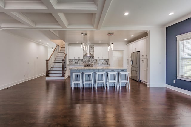 kitchen featuring white cabinetry, decorative light fixtures, an island with sink, stainless steel fridge with ice dispenser, and wall chimney exhaust hood