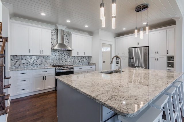 kitchen featuring a spacious island, decorative light fixtures, stainless steel appliances, sink, and wall chimney range hood