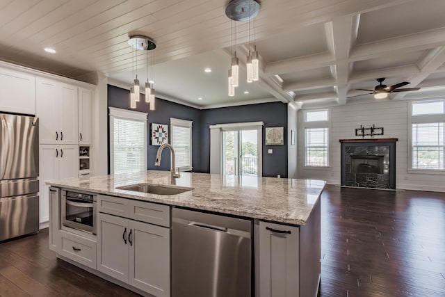 kitchen with decorative light fixtures, a fireplace, appliances with stainless steel finishes, an island with sink, and sink