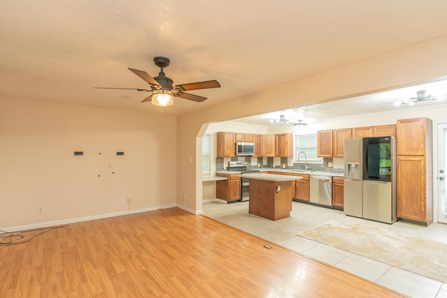 kitchen with light wood-type flooring, sink, a center island, ceiling fan, and appliances with stainless steel finishes