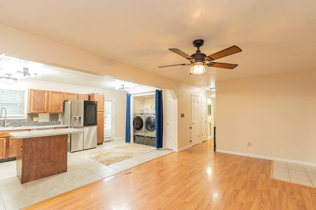 kitchen with light wood-type flooring, stainless steel fridge, ceiling fan, a kitchen island, and washer and clothes dryer