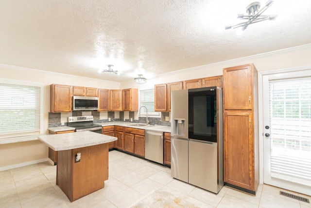 kitchen with a kitchen island, light tile patterned floors, stainless steel appliances, ornamental molding, and sink