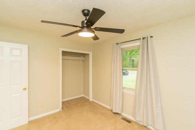 unfurnished bedroom with a textured ceiling, a closet, ceiling fan, and light carpet