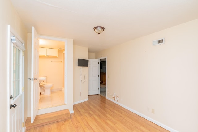 unfurnished bedroom with a closet, a spacious closet, ensuite bathroom, and light hardwood / wood-style floors