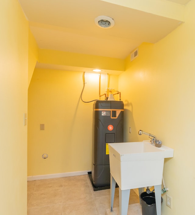 clothes washing area with water heater, light tile patterned floors, and sink