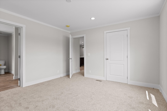 unfurnished bedroom featuring crown molding, ensuite bathroom, and light carpet