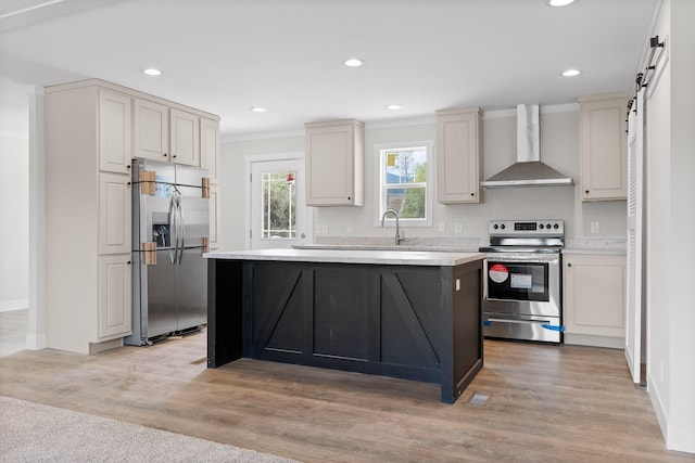 kitchen with light wood-type flooring, stainless steel appliances, wall chimney exhaust hood, crown molding, and a barn door