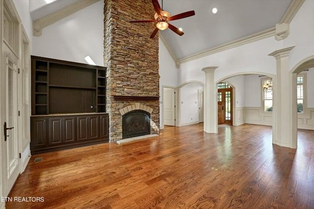 unfurnished living room featuring ceiling fan, decorative columns, wood-type flooring, a stone fireplace, and high vaulted ceiling