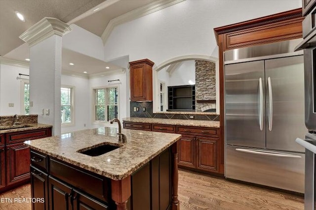 kitchen with built in fridge, vaulted ceiling, a center island with sink, light hardwood / wood-style flooring, and sink