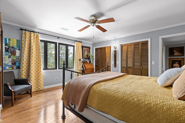 bedroom featuring light hardwood / wood-style flooring, two closets, ceiling fan, and ornamental molding