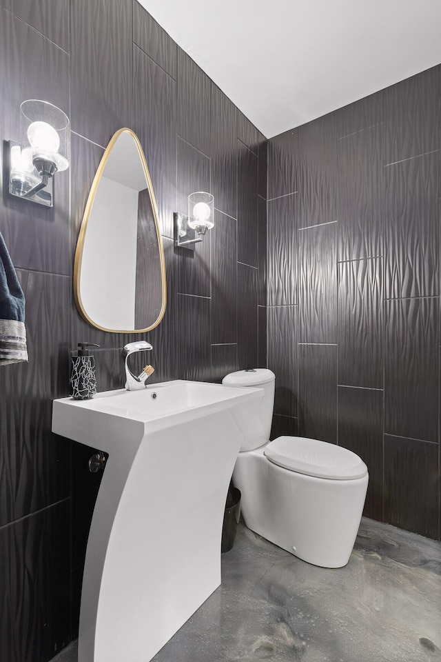 bathroom with tile walls, concrete floors, and toilet