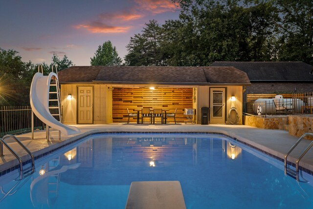 pool at dusk with a diving board, a water slide, and a patio area