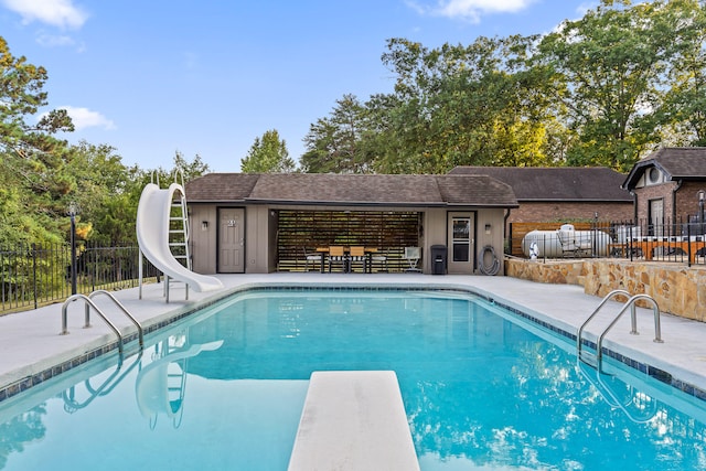 view of swimming pool featuring a diving board, a water slide, and a patio area