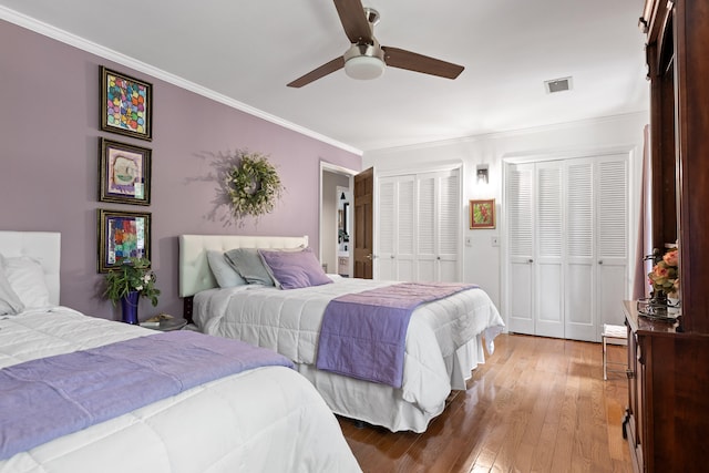 bedroom with two closets, ornamental molding, ceiling fan, and dark wood-type flooring