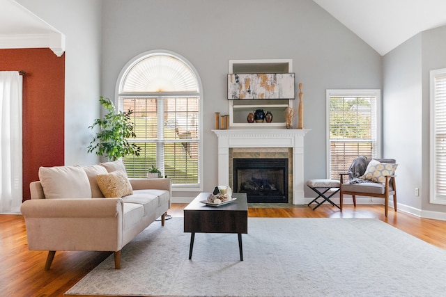 living room with light hardwood / wood-style flooring, crown molding, high vaulted ceiling, and a tile fireplace