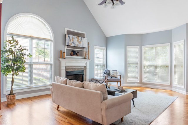 living room featuring a tile fireplace, a healthy amount of sunlight, light hardwood / wood-style floors, and ceiling fan