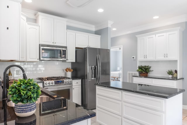 kitchen with appliances with stainless steel finishes, dark stone countertops, tasteful backsplash, white cabinets, and a center island