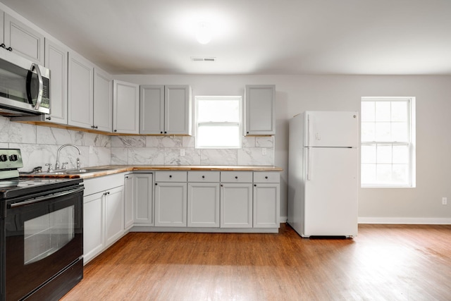 kitchen with backsplash, range with electric stovetop, white refrigerator, and light wood-type flooring