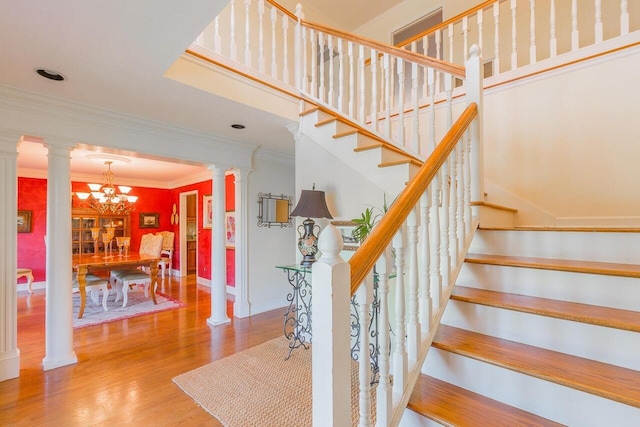 staircase with ornamental molding, an inviting chandelier, hardwood / wood-style floors, and decorative columns