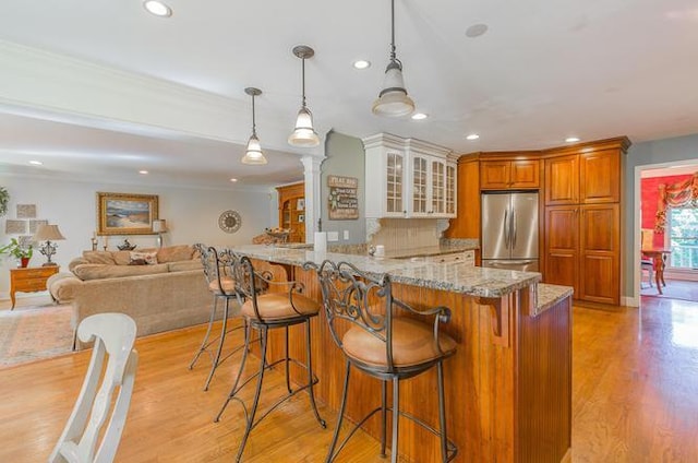 kitchen with pendant lighting, stainless steel fridge, light hardwood / wood-style flooring, light stone counters, and kitchen peninsula