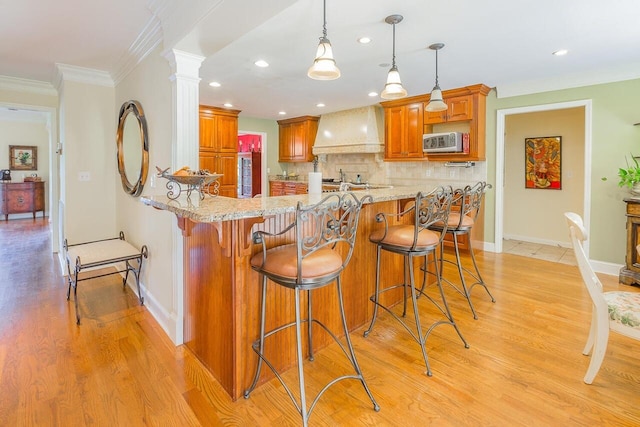 kitchen featuring decorative columns, a kitchen bar, light hardwood / wood-style floors, and custom range hood