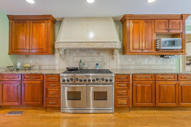 kitchen featuring tasteful backsplash, stainless steel range, premium range hood, and light hardwood / wood-style floors