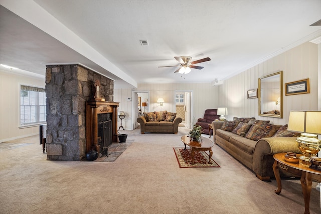 living room featuring crown molding, light colored carpet, ceiling fan, and a stone fireplace