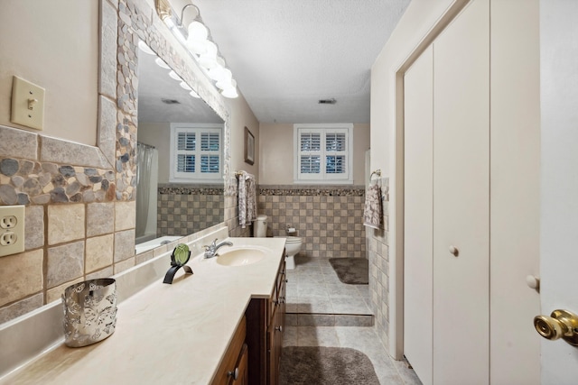 bathroom with tile patterned flooring, toilet, tile walls, vanity, and a textured ceiling