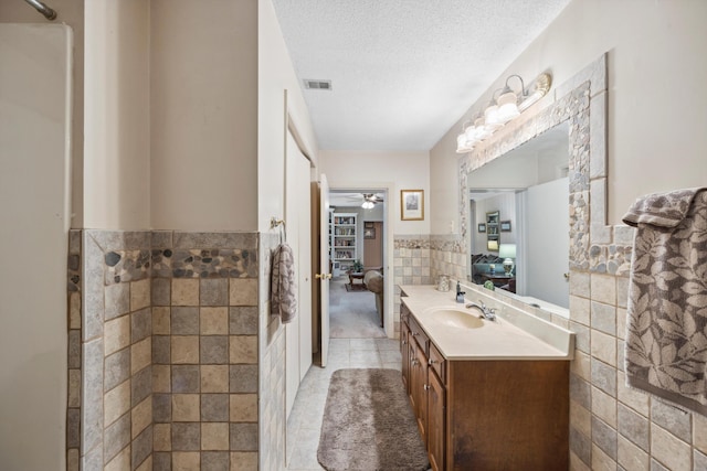 bathroom featuring a textured ceiling, vanity, tile walls, tile patterned floors, and a shower