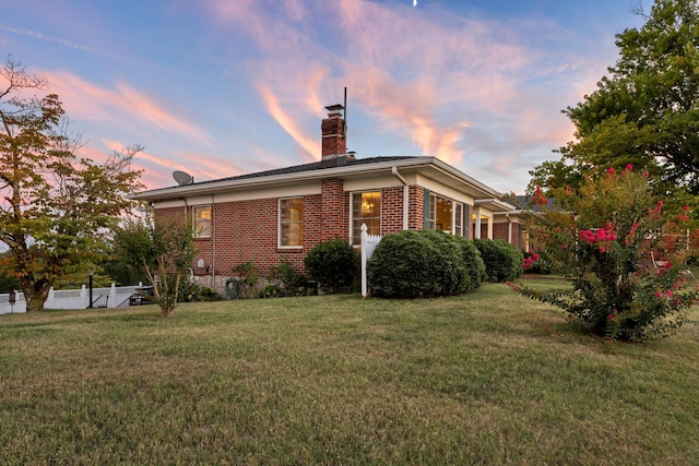 back house at dusk featuring a lawn