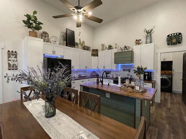 kitchen with dark wood-type flooring, tasteful backsplash, black fridge, washer / dryer, and white cabinets